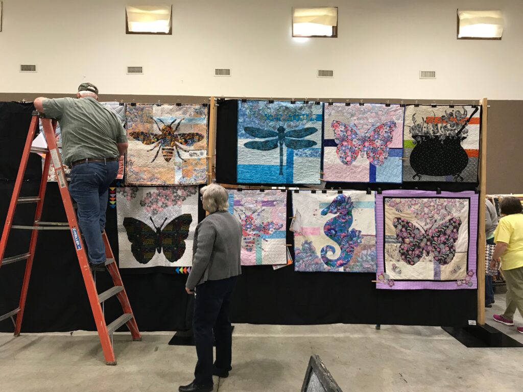 Image of wall hanging quilts being hung in quilt show.